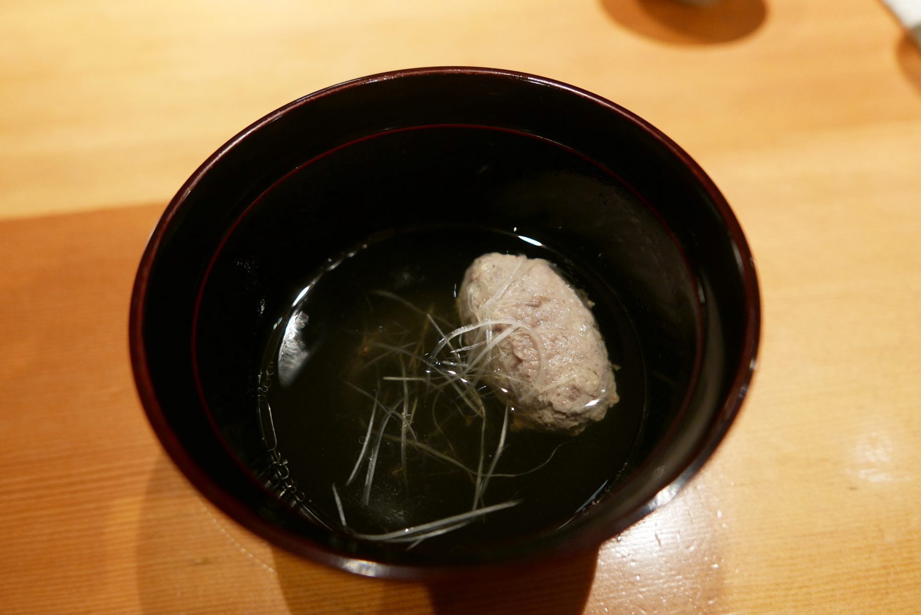 Sardine dumpling in clear soup with thinly sliced leek and a bit of ginger.